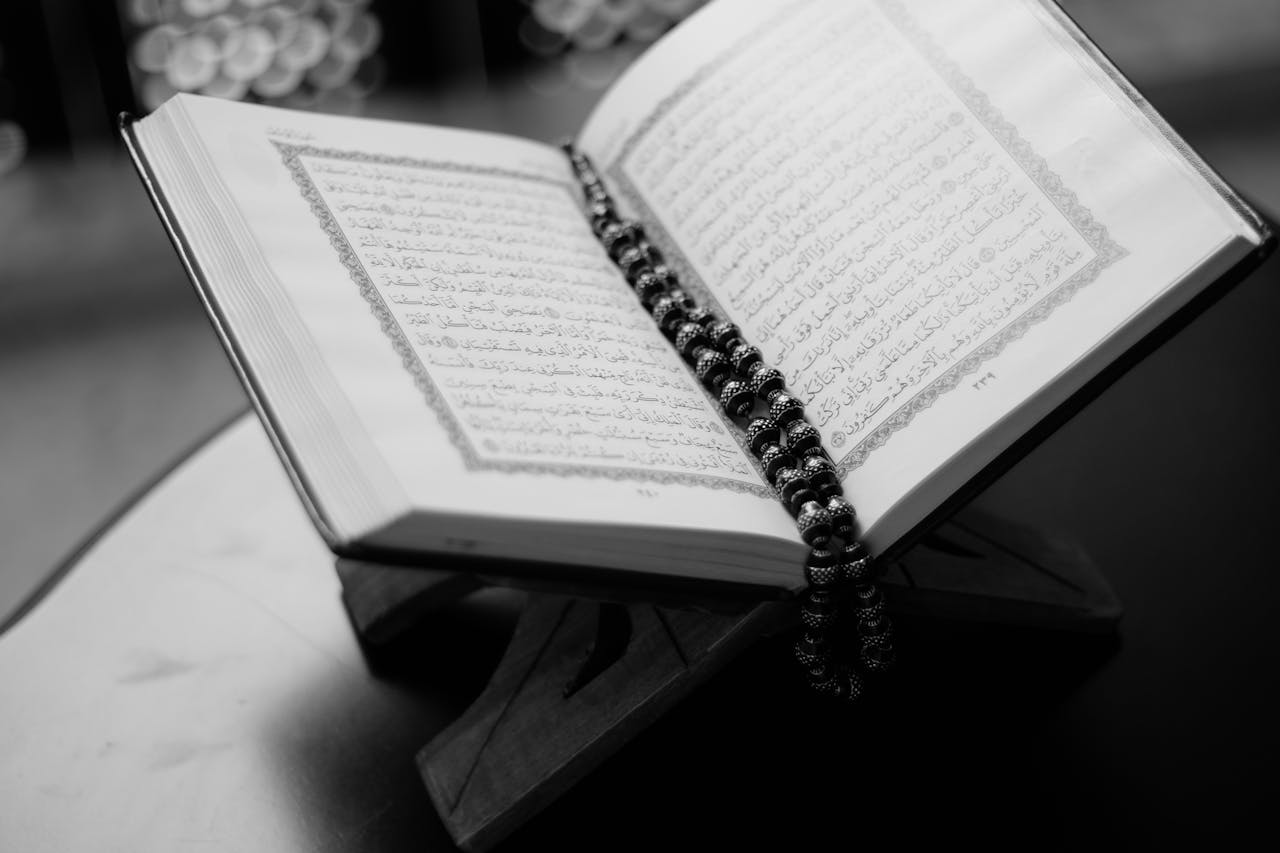 creative A black and white close-up of an open Quran on a wooden stand with prayer beads, symbolizing Islamic faith and devotion.